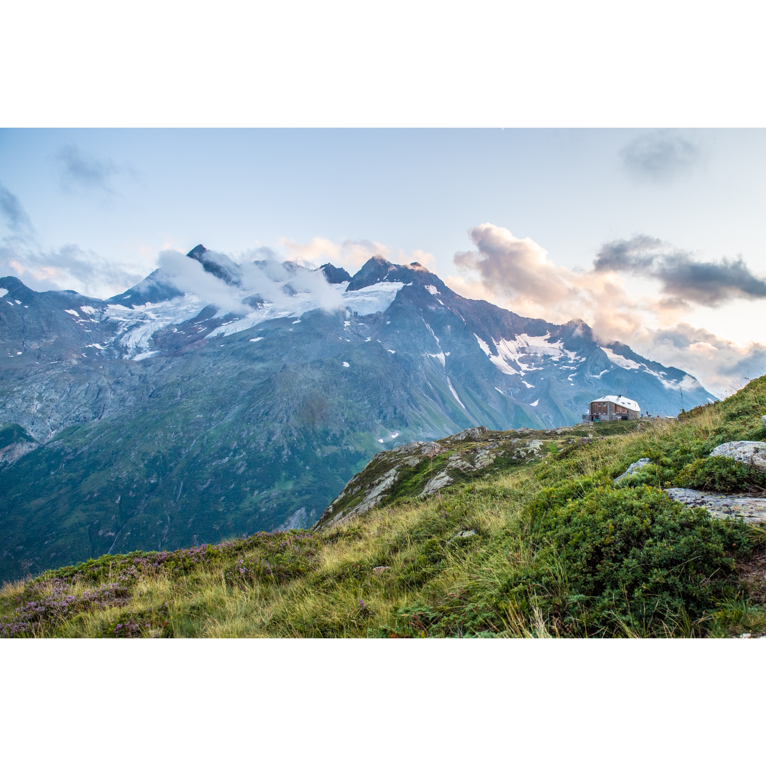 View from one mountain to another mountain of the Alps in summer sunshine. With green meadow. The top of the opposite mountain is still white.